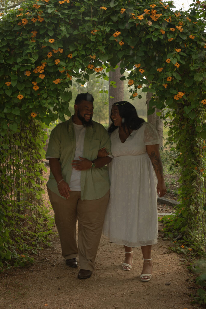 A couple holds hands while walking through a wooded garden path at Mercer Botanical Gardens during their engagement photoshoot.
