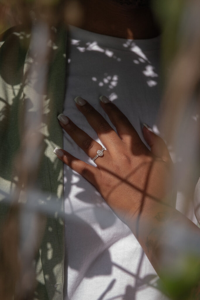 A close-up detail of an engagement ring resting on a partner’s chest with soft leaf shadows at a Houston garden session.