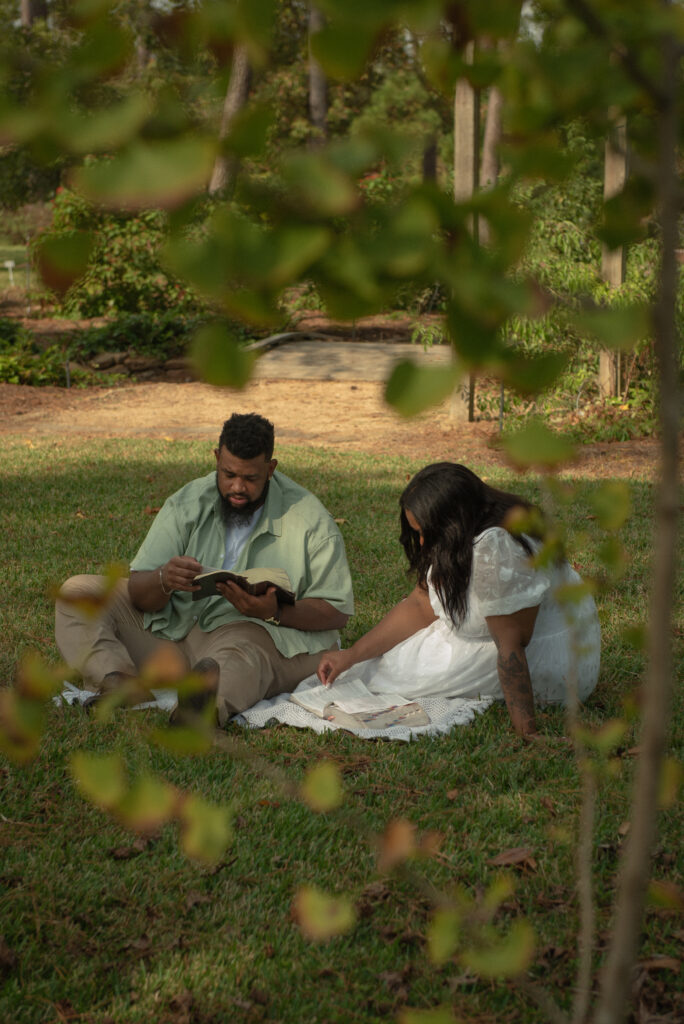 A couple sits on a blanket reading their Bibles together during a Christian engagement session in a quiet area of Mercer Botanical Gardens