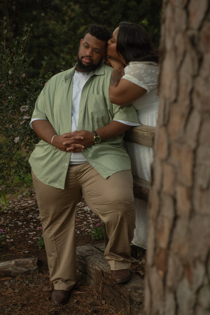 A couple shares a peaceful moment on a wooden fence surrounded by greenery during their engagement photos at a botanical garden.