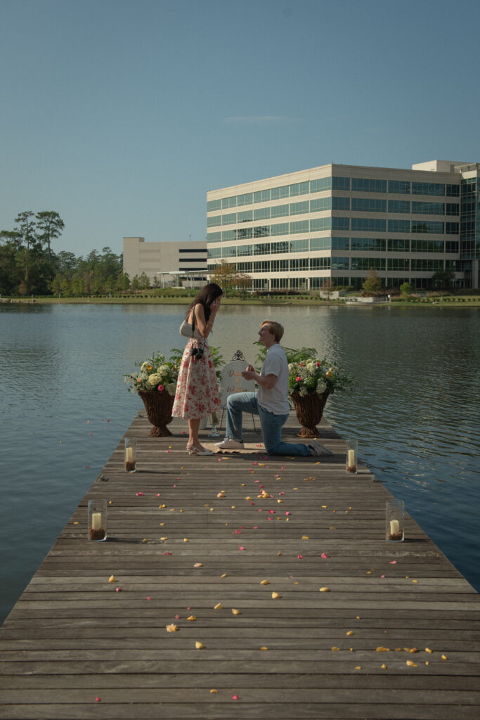 Emotional surprise proposal at Lake Woodlands with one partner kneeling on a dock surrounded by florals and candles