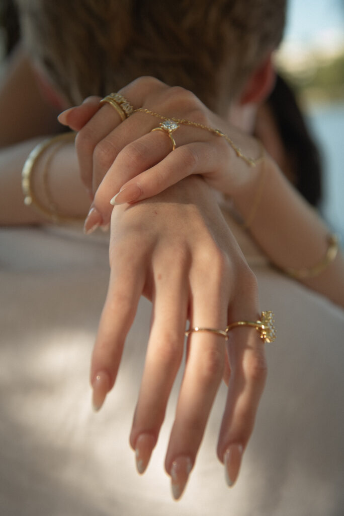 Close-up of engagement ring and gold jewelry as a couple embraces during a romantic proposal session