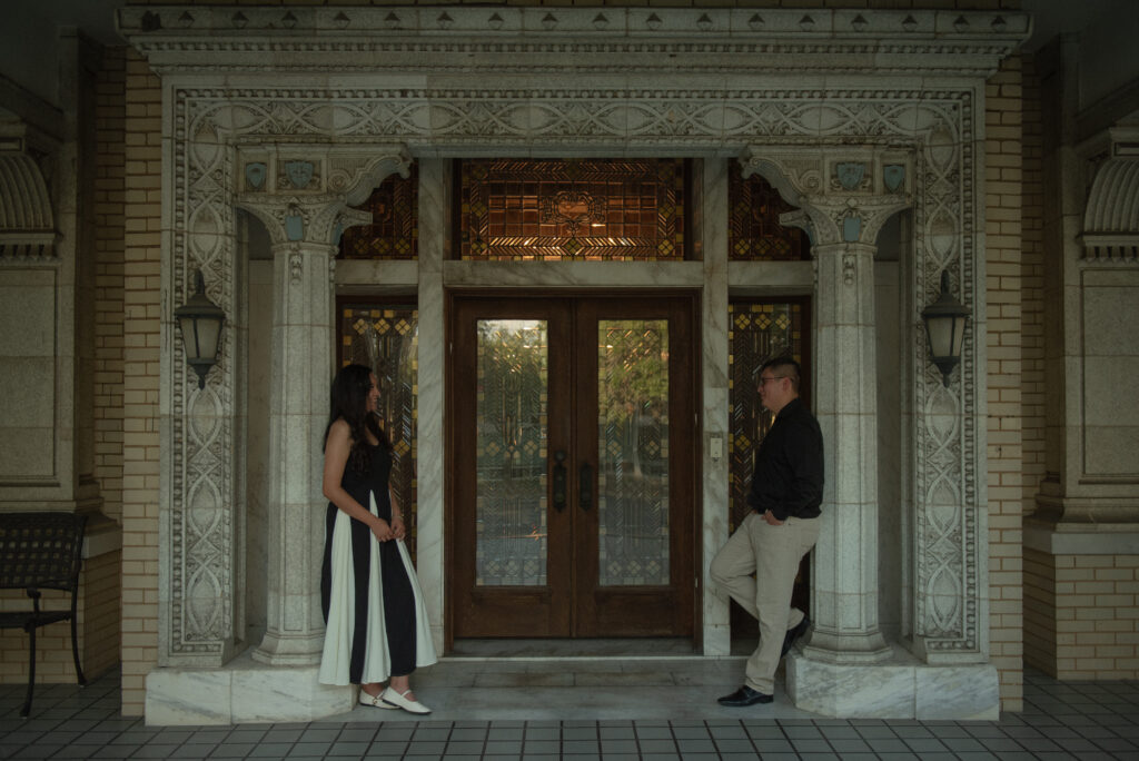 A couple standing across from each other in front of an ornate doorway
