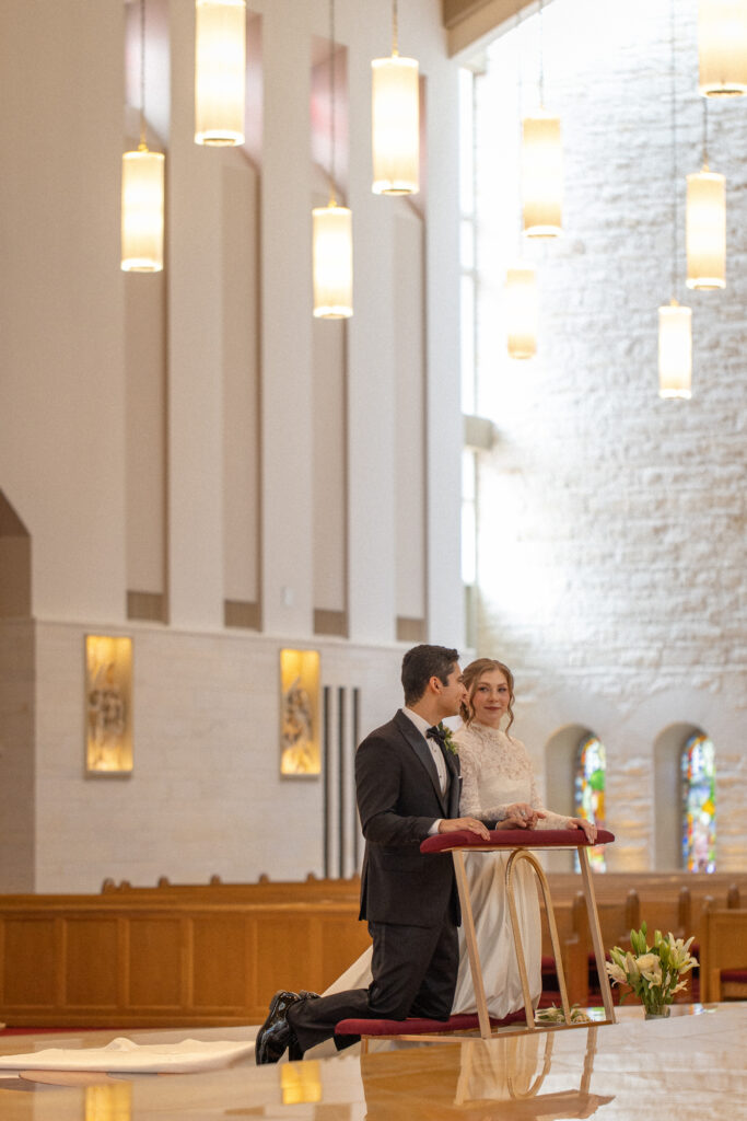 A bride and groom kneel in prayer at the altar during their church wedding ceremony.