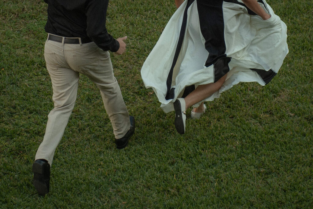 A candid photo of a couple running together across a grassy lawn.