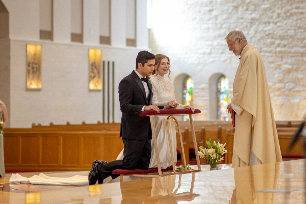 bride and groom kneel together at the front of the church during their wedding ceremony.