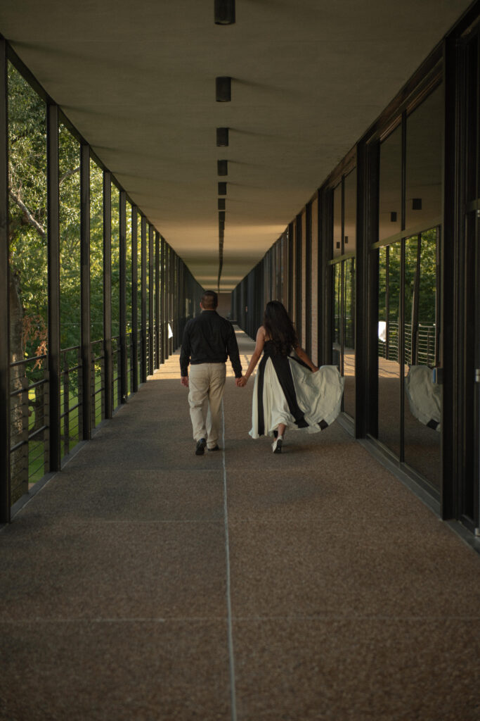 A couple walking hand in hand down a long covered walkway.