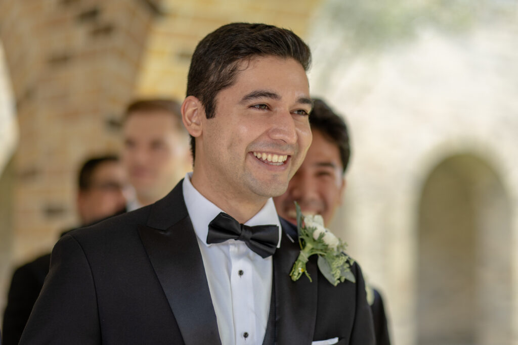 A groom smiles while standing with his groomsmen during wedding portraits in formal tuxedos.