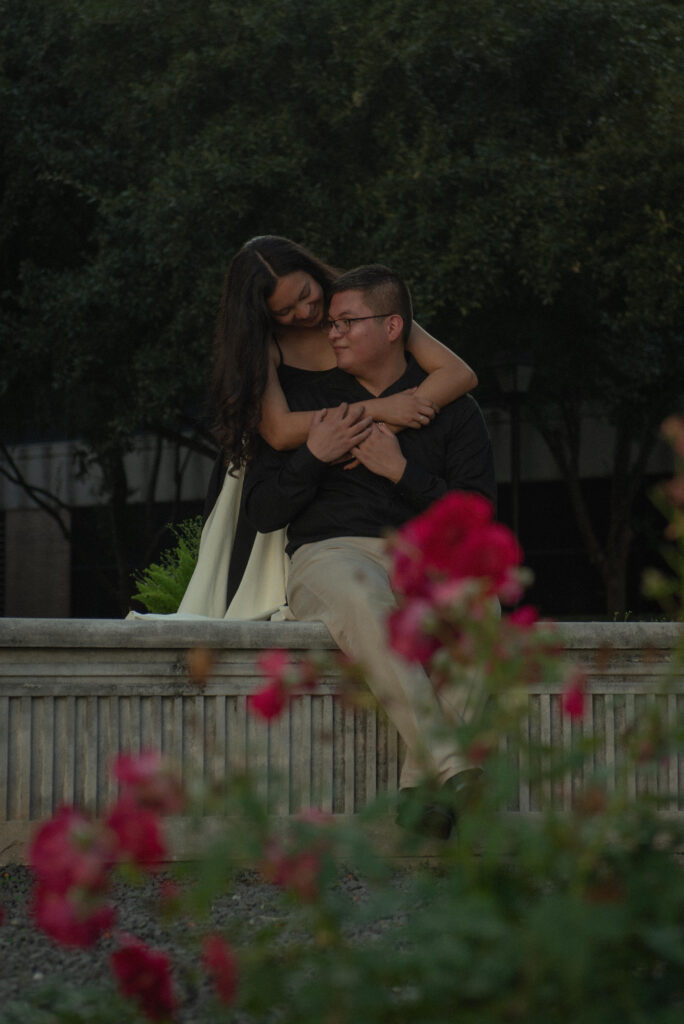 A woman leaning affectionately over her partner while sitting near a garden