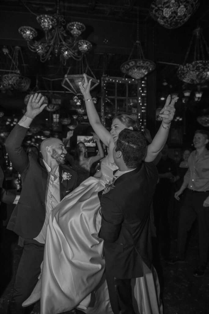 Bride laughs as guests lift her up during the wedding celebration.