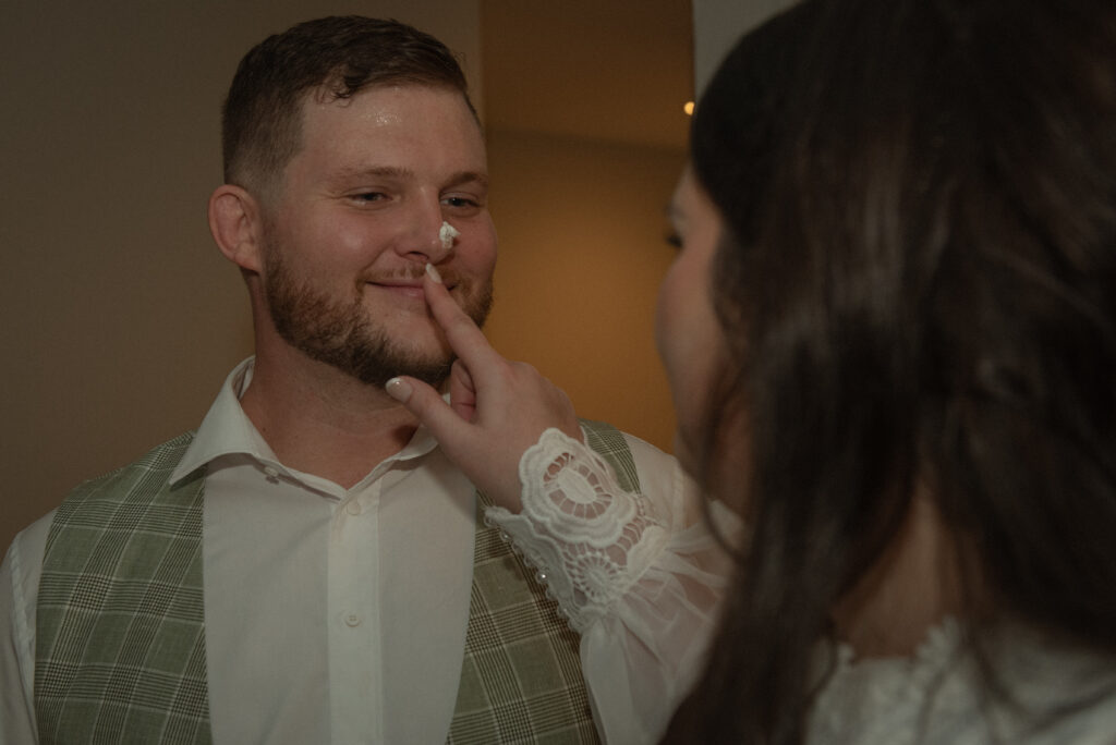 Candid moment of an eloping couple laughing together during cake cutting indoors