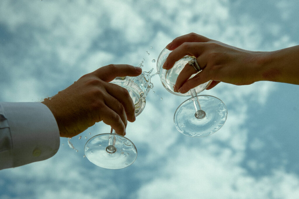 Couple raising champagne glasses toward the sky during a sunny celebratory toast after their courthouse elopement