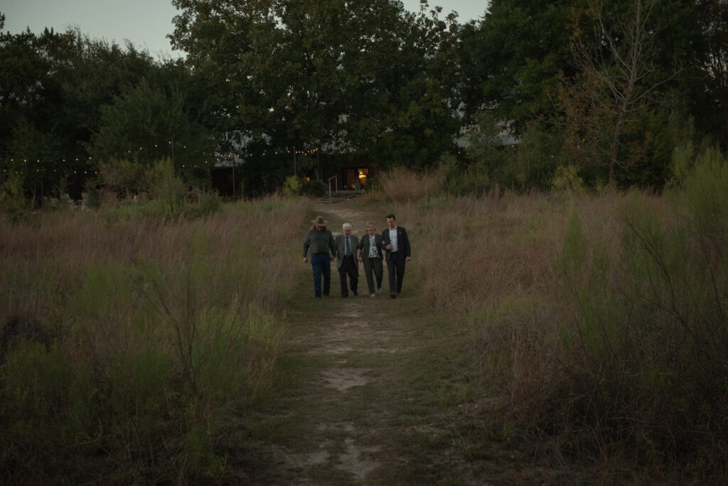 Family members walking together toward an outdoor wedding ceremony in the Texas Hill Country at sunset.
