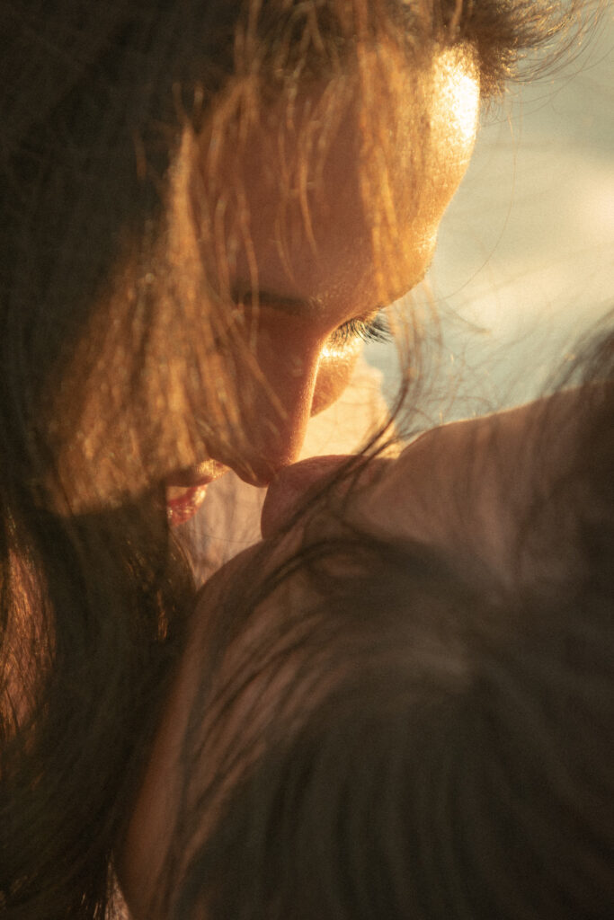 Warm close-up photo of a couple sharing a kiss in golden hour light.