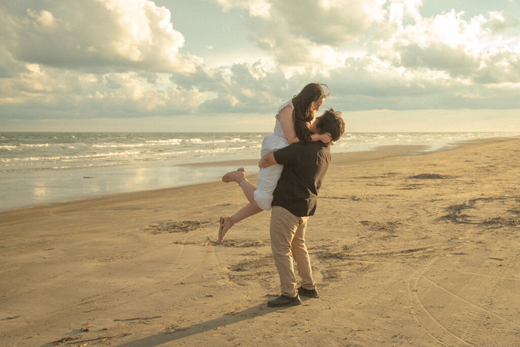 Man lifting his fiancée during a sunset engagement session on the beach.