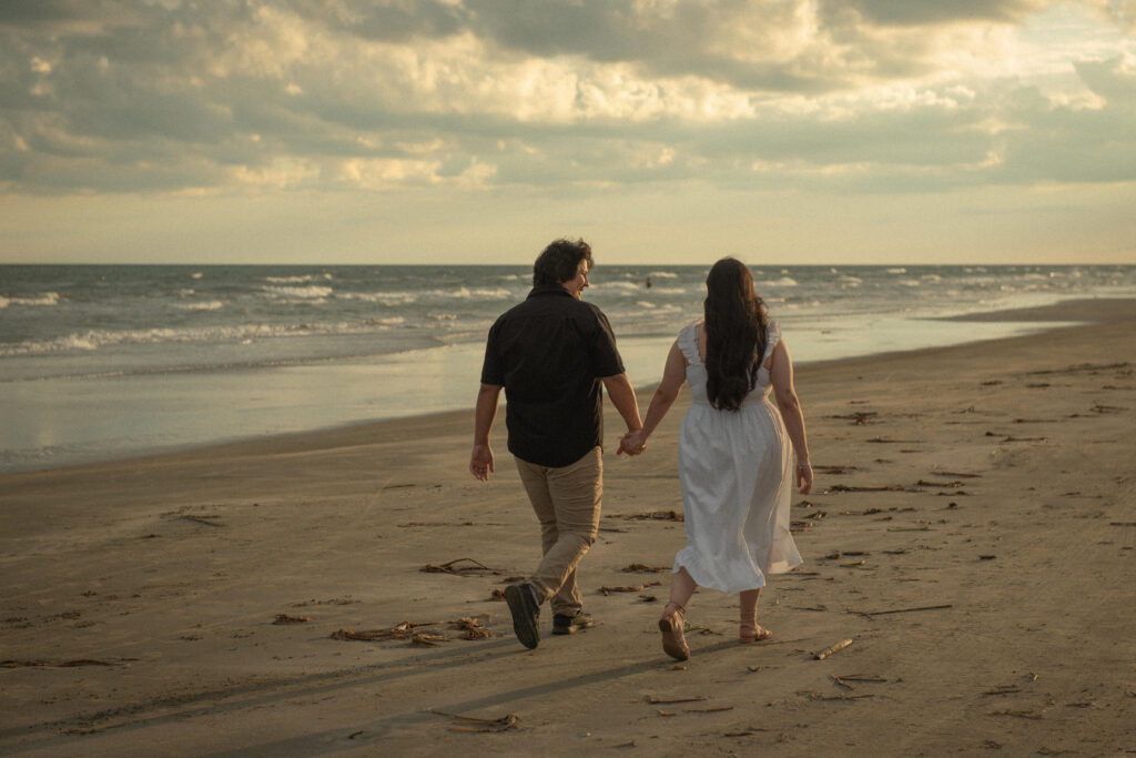 Engaged couple walking hand in hand along the shoreline at sunset in Galveston.