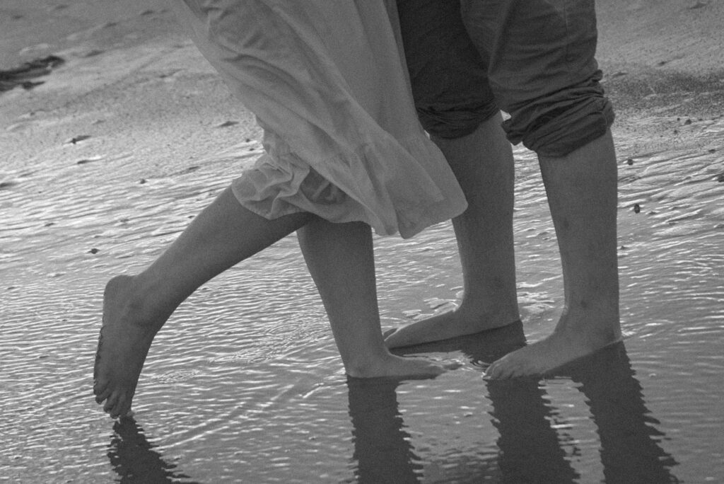 Close-up of couple’s bare feet standing in shallow water at the beach.