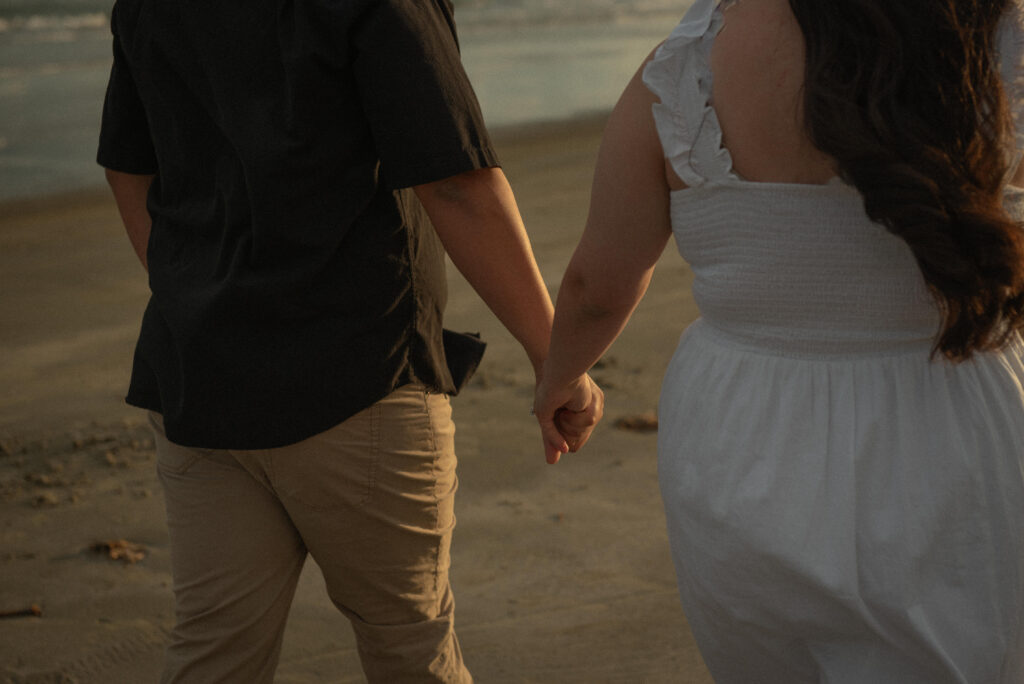 Detail photo of an engaged couple holding hands while walking on the beach.