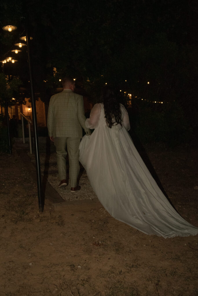 Newlyweds walking together under string lights during a Texas Hill Country elopement evening