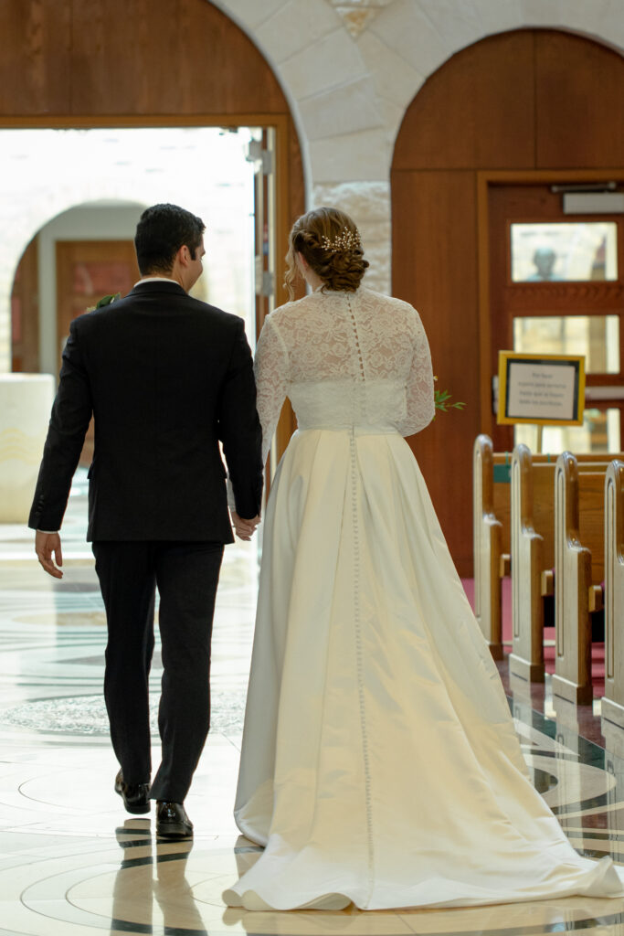 Bride and groom walk hand in hand toward the church doors after their ceremony in Houston.