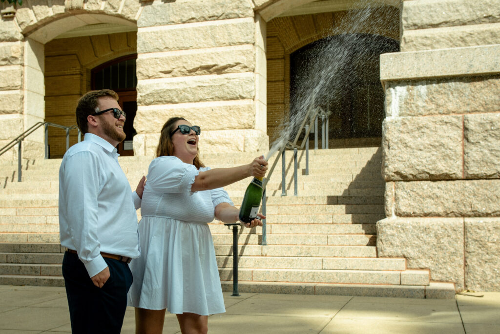 Couple celebrating their Houston courthouse elopement by popping champagne on the steps of the historic 1910 Courthouse.