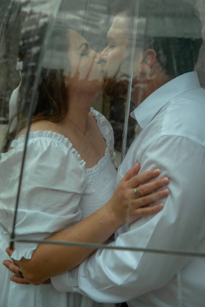 A couple sharing a kiss behind a clear umbrella during their rainy courthouse elopement session.