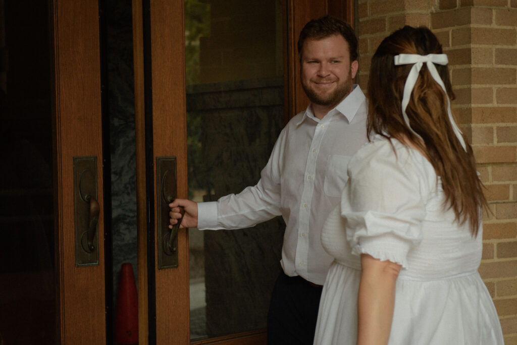 A couple holding the courthouse door open as they enter the historic building for their elopement.