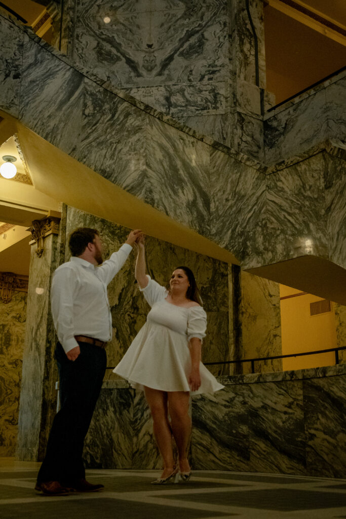 Couple sharing a joyful dance inside the Houston 1910 courthouse surrounded by marble architecture.