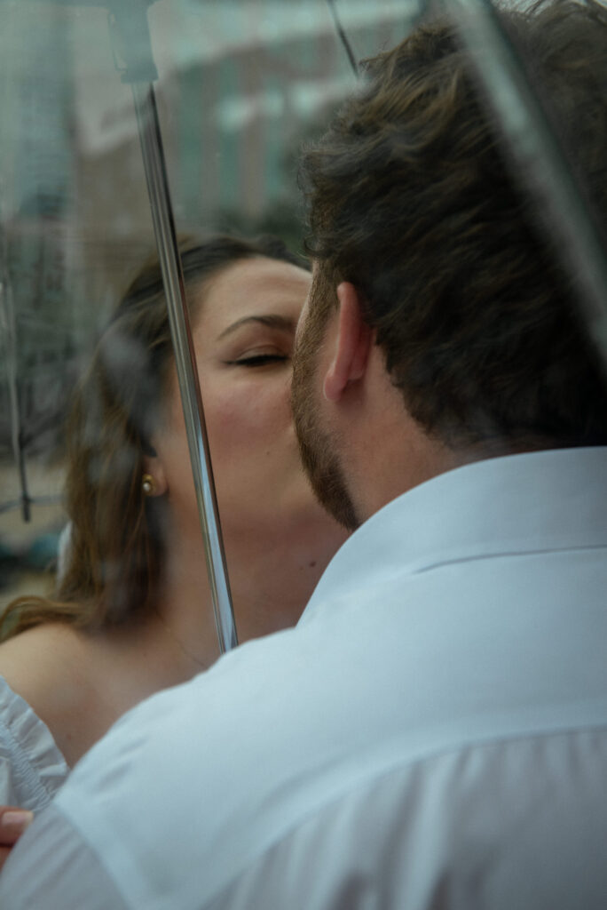 Couple sharing a romantic kiss under a clear umbrella during a rainy Houston courthouse elopement