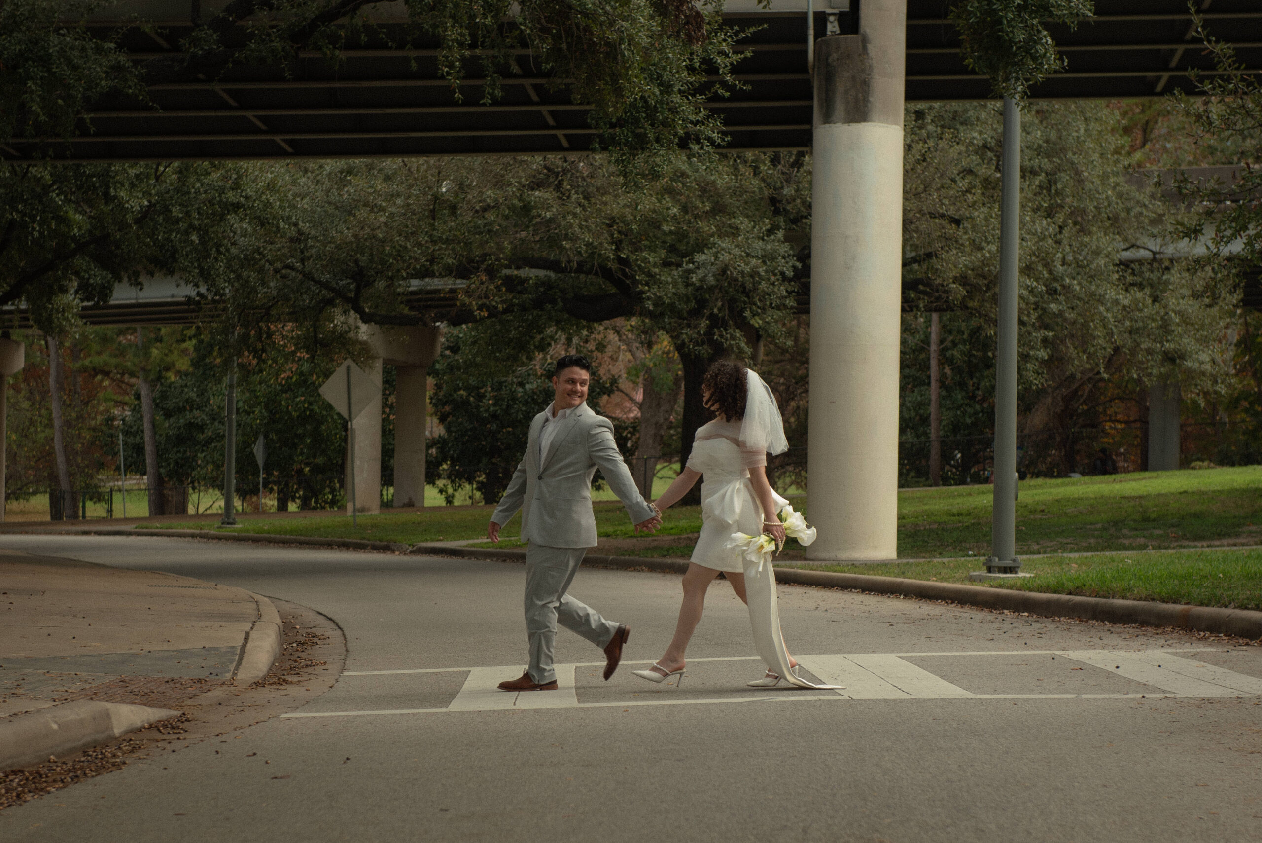 Newlywed couple holding hands while crossing the street during downtown Houston elopement portraits.