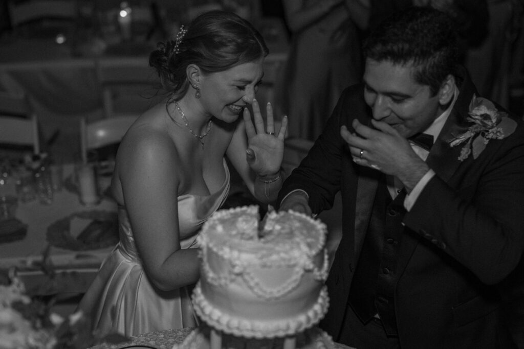 Bride and groom laugh together while cutting their tiered wedding cake.