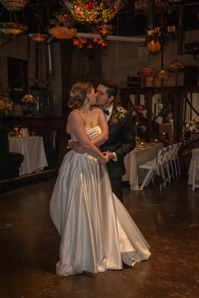 Bride and groom share their first dance surrounded by antique stained-glass lamps.