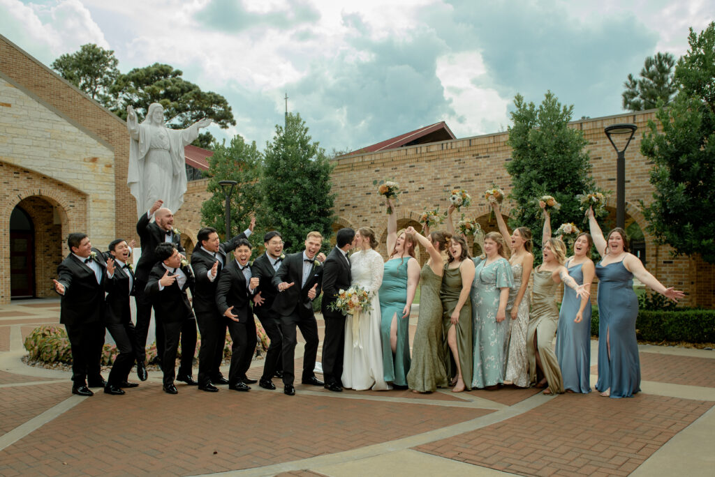 Full wedding party cheering with the bride and groom outside the church.
