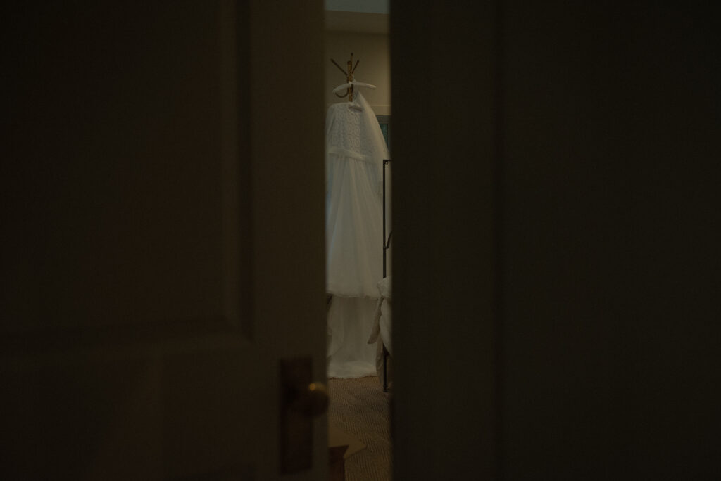 Wedding dress hanging indoors during an intimate elopement, photographed in natural light with a moody, cinematic feel.