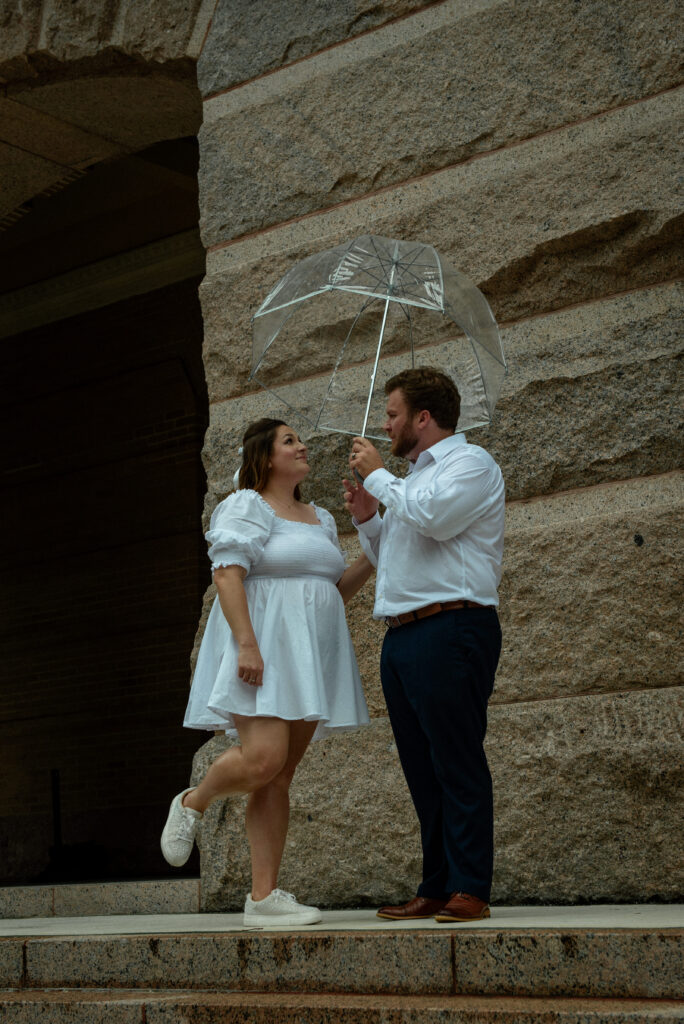 A couple standing under a clear umbrella outside the Houston courthouse during a rainy elopement day.