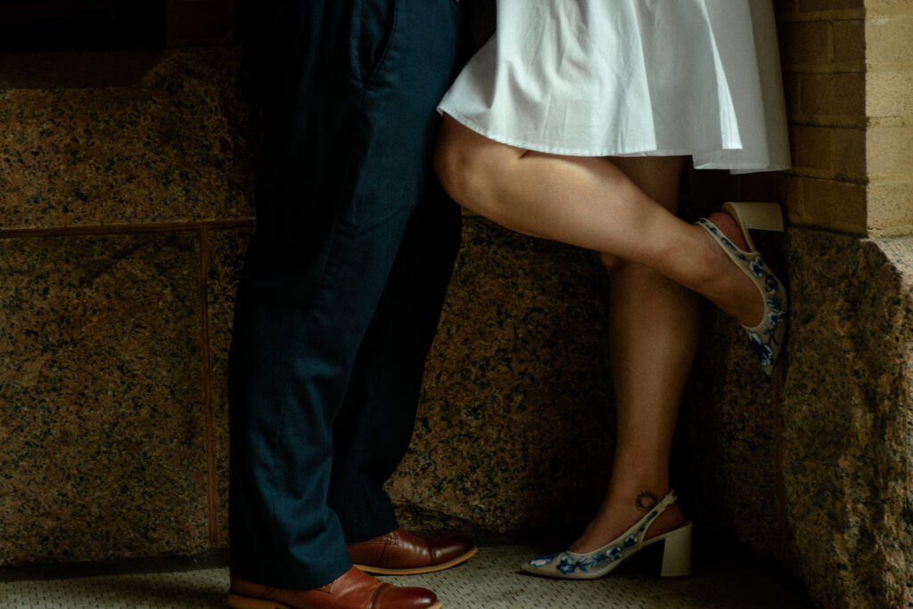 A detail photo of a couple standing close together, highlighting their shoes and the courthouse stonework.