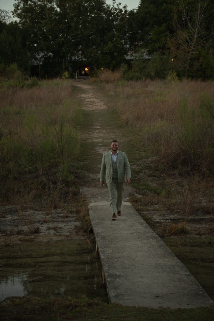Groom walking along a stone path toward an outdoor Hill Country elopement ceremony in Texas.