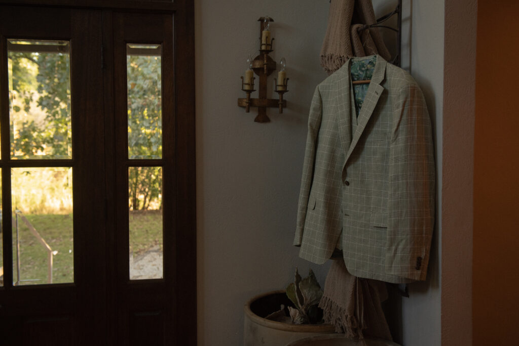 Groom’s wedding suit hanging by a doorway during a Texas Hill Country elopement, captured in a cinematic documentary style.