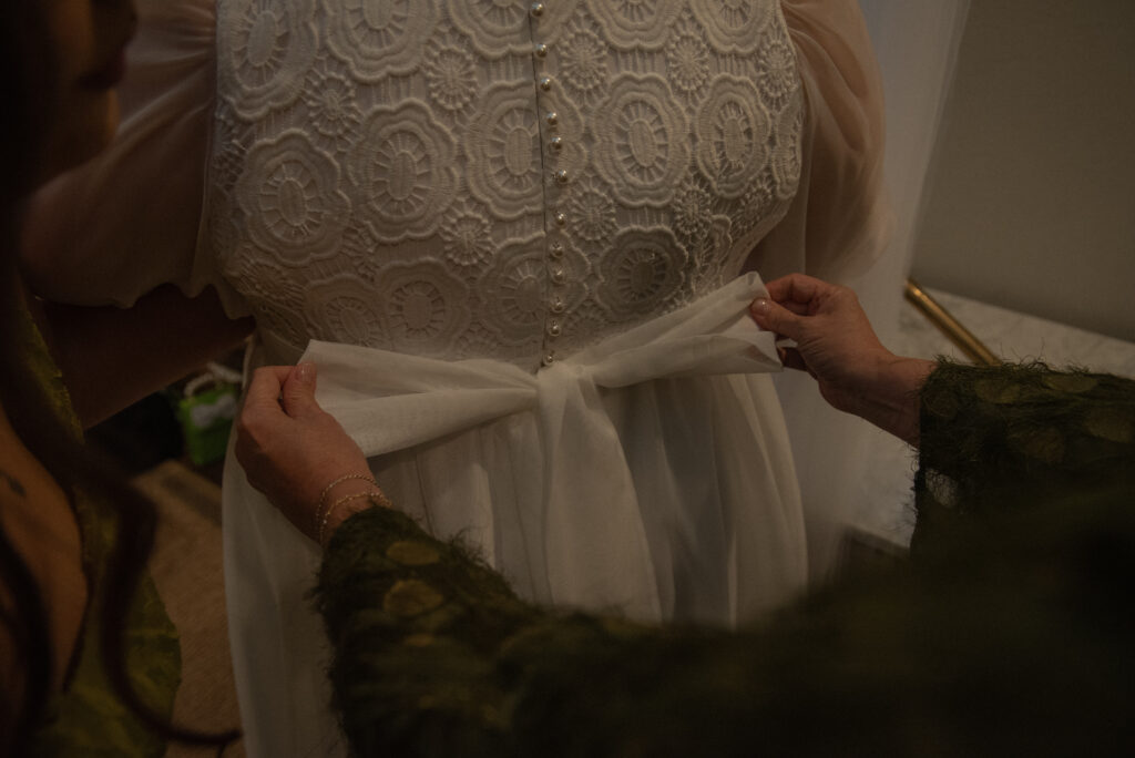 Close-up of family members helping fasten a wedding dress during a small, intimate elopement ceremony.