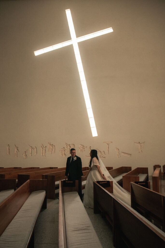 Couple standing inside a modern chapel beneath a large illuminated cross