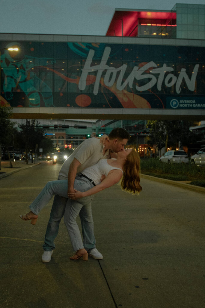 Engagement photo of a couple sharing a dip kiss on a downtown Houston street at dusk.