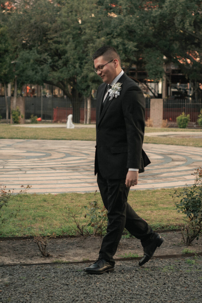 Groom walking through a campus courtyard with a circular stone pattern, classic wedding portrait outdoors.