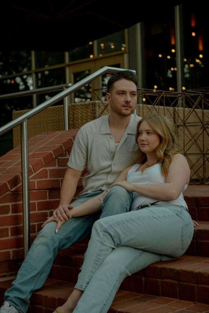 Engagement photo of a couple sitting close together on brick steps in Houston during evening light.