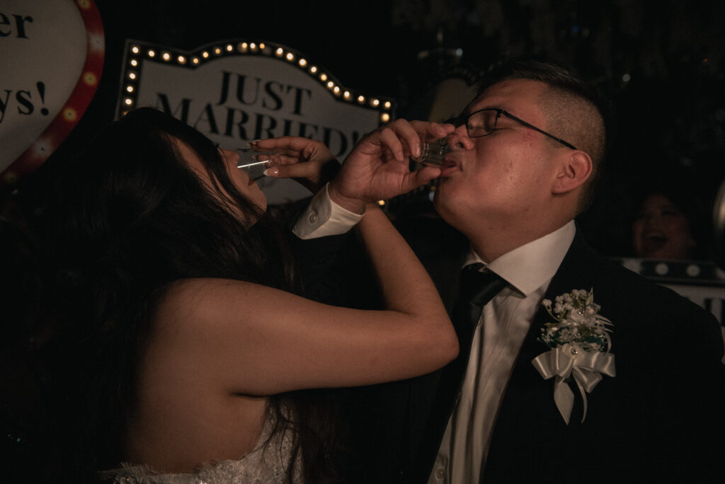 Newlyweds taking celebratory shots in front of a “Just Married” sign.