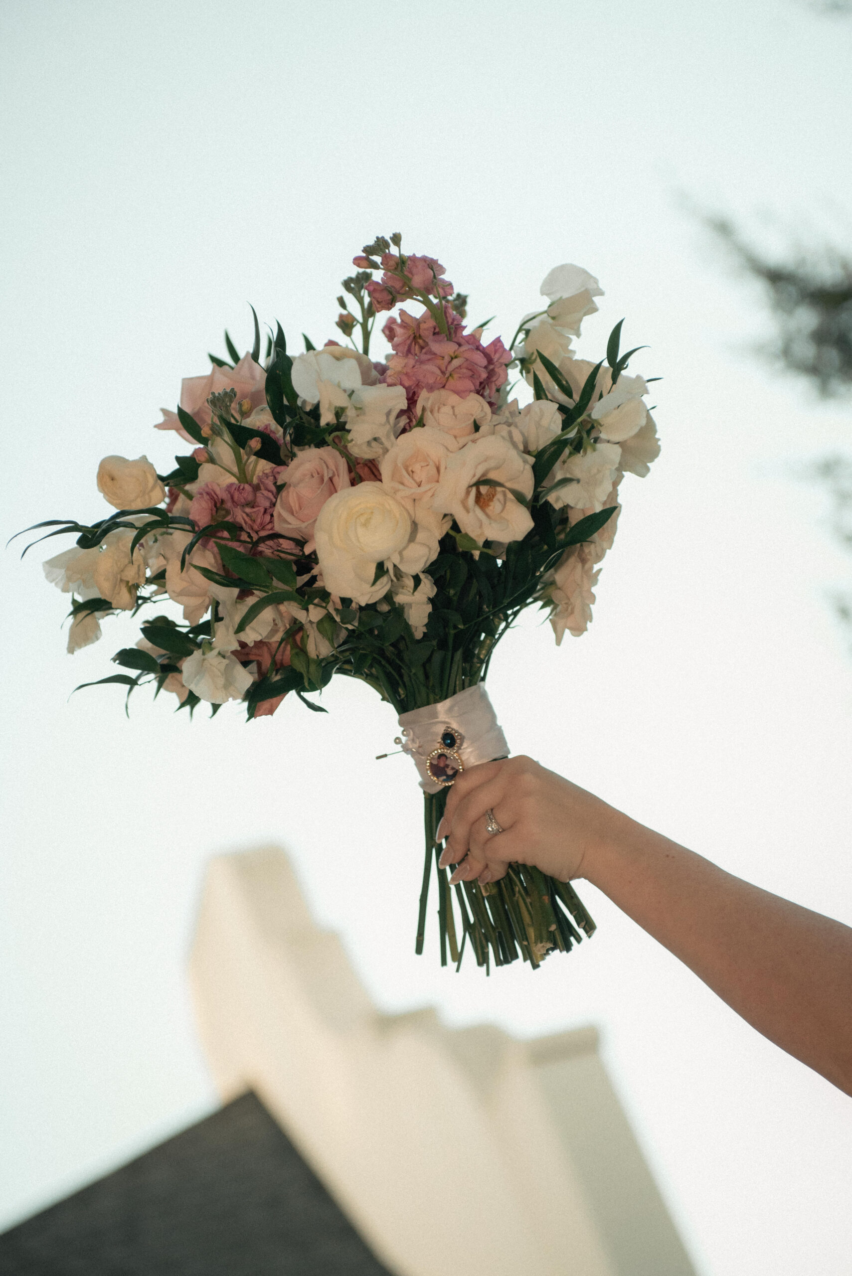 Bride holds up a pastel wedding bouquet against the sky outside a Houston venue.