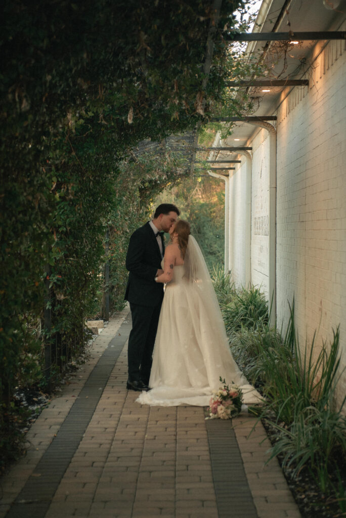 Couple kissing in a garden walkway during wedding portraits with soft evening light.