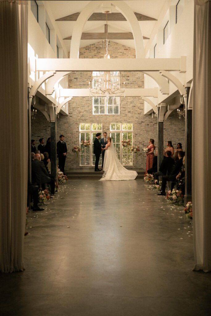 Wide photo of an indoor wedding ceremony with guests seated and the couple at the altar.