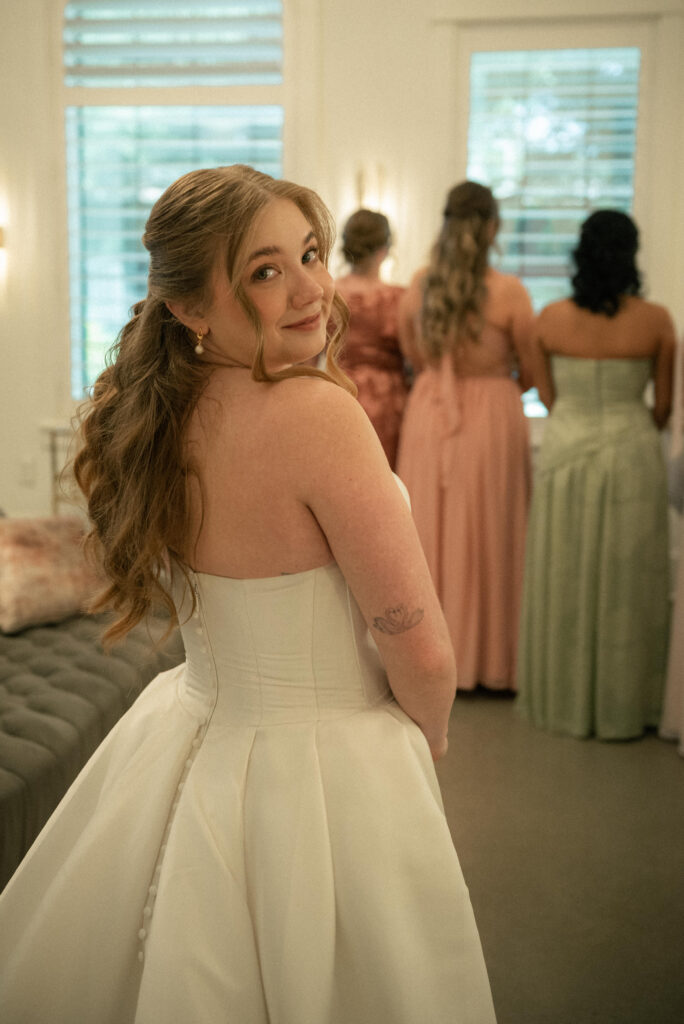 Bride looking back over her shoulder during getting ready with bridesmaids in the background.