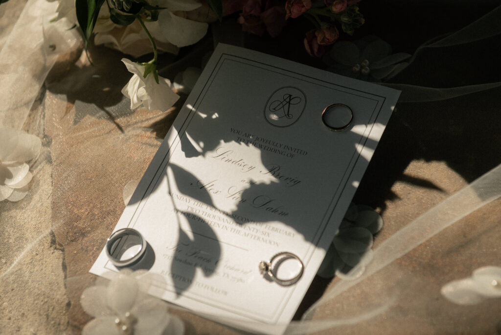 Wedding invitation suite flat lay with wedding rings, florals, and soft natural light.