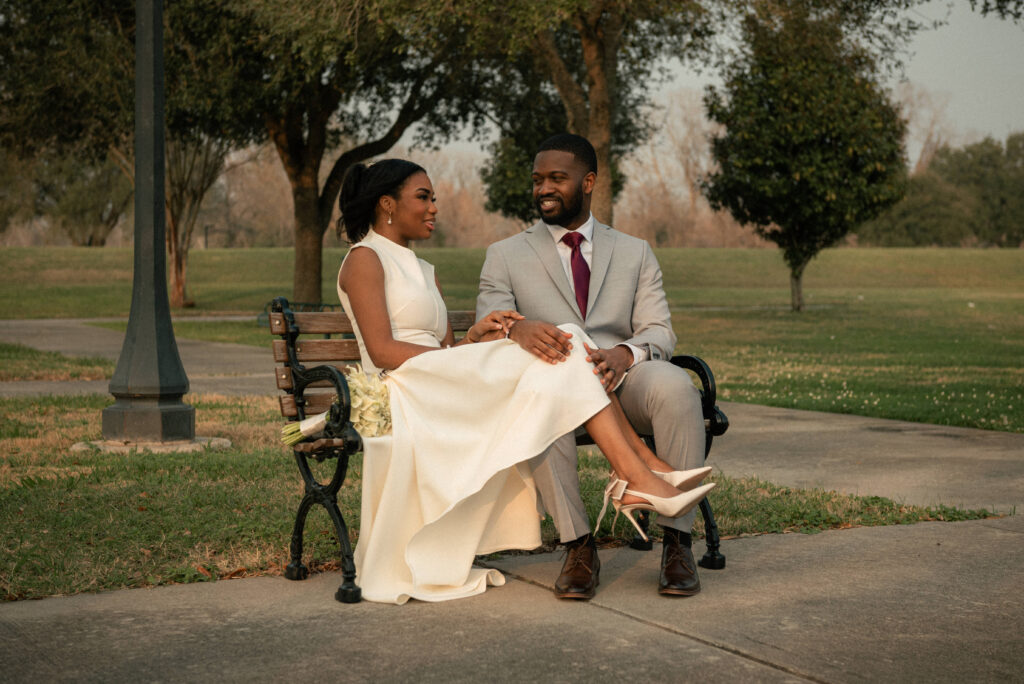 Couple sitting on a park bench after a courthouse wedding with bouquet nearby.
